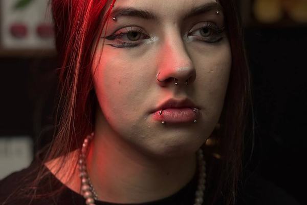 Asmuo raudonai apšviestoje piercingo studijoje su poriniais lūpų auskarais, septumo žiedu ir antakių vėrimais – pavyzdys, kaip apgalvotas vėrimų išdėstymas dera su kasdieniu stiliumi.