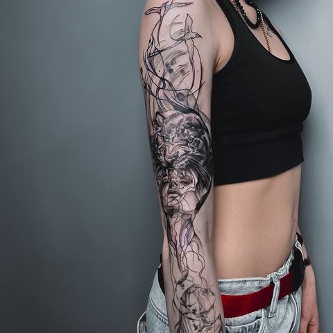 Juodai pilka rankovės tatuiruotė su portretiniais ir dekoratyviniais motyvais, sujungtais į vientisą, detalią kompoziciją.