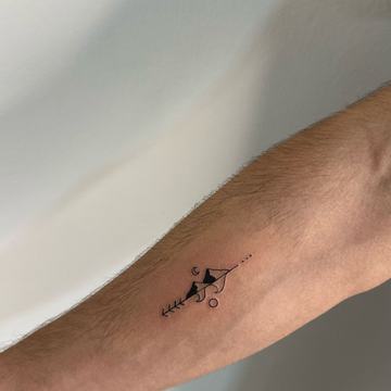 Maža juodo rašalo geometrinė tatuiruotė ant dilbio: plonos linijos, trikampis, apskritimai ir šakelės/strėlės motyvas—minimalistinio blackwork stiliaus pavyzdys mažam formatui matomoje vietoje.