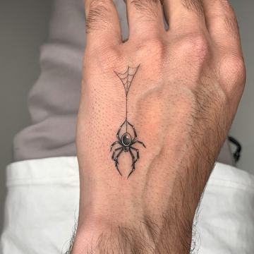 Maža juodo rašalo voro tatuiruotė ant plaštakos, su plonu voratinklio siūlu—minimalistinio/blackwork stiliaus pavyzdys mažam formatui matomoje vietoje.