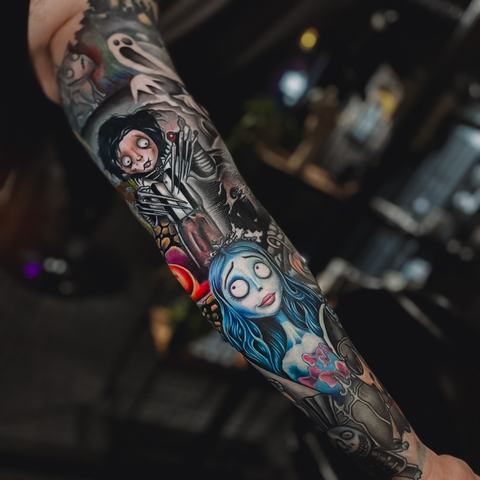 Spalvinga rankovės tatuiruotė išsiskiria ryškiais mėlynais ir raudonais elementais, dinamiškais personažų motyvais ir kontrastingomis detalėmis, kurios visą kompoziciją paverčia gyva ir energinga.