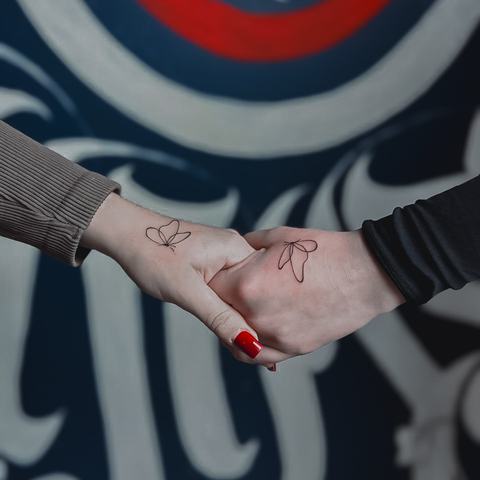 Subtili raudonos gijos tatuiruotė ant plaštakos, išsiskirianti lengvu linijiniu piešiniu ir minimalistine kompozicija.
