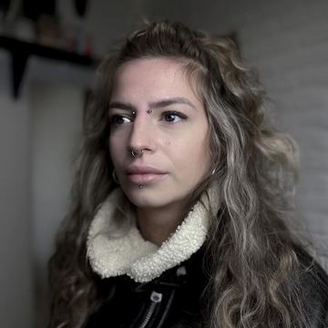 Portrait of a person in a studio with a septum ring, bridge piercing between the eyebrows, and an off-center labret stud, illustrating professional facial piercing options in Panevėžys.