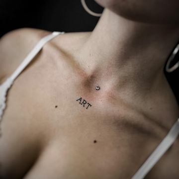 Artimo plano asmens krūtinės sritis su dermaliniu (paviršiniu) vėrimu virš krūtinkaulio – subtilus kristalinis papuošalas ir tatuiruotė „ART“, iliustruojantys saugų, profesionalų kūno vėrimą ir tinkamo pradinio papuošalo parinkimą VeAn studijoje Šiauliuose.