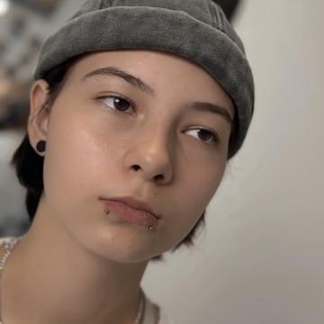 Close-up three-quarter portrait of a person in a beanie with snake-bite lip studs and a black stretched earlobe plug, showcasing professional facial and ear piercing options in Klaipėda.