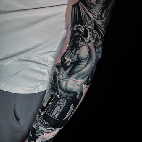 A detailed black and grey forearm tattoo featuring a wolf portrait with realistic shading