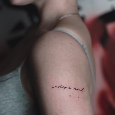 A subtle script tattoo on the upper arm, kept minimal with fine lettering and a clean, understated placement.