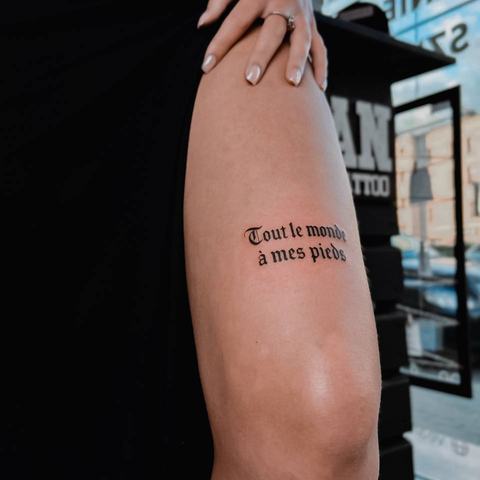 A minimalist text tattoo on the thigh with a short black inscription