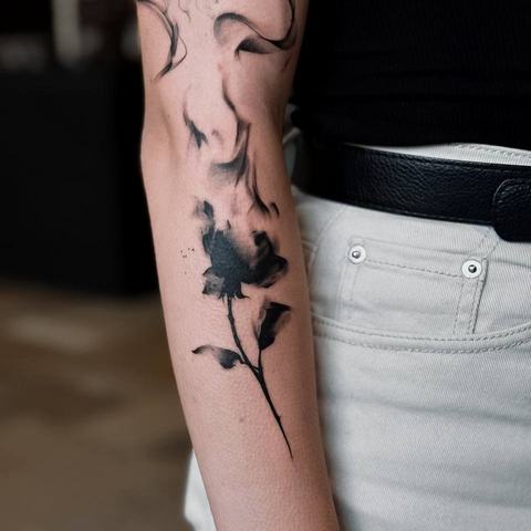 A delicate floral forearm tattoo with fine line leaves and a small blue flower