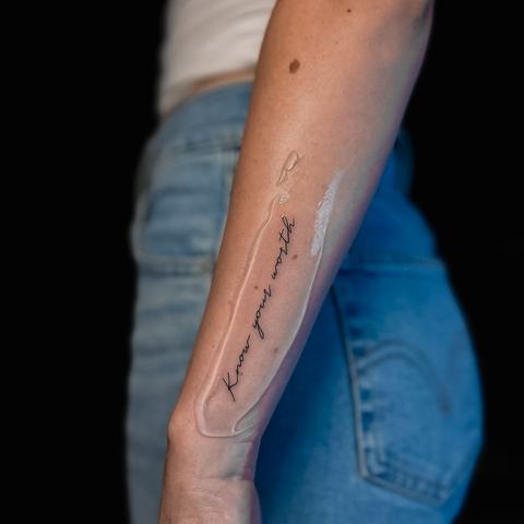 A slender fine-line forearm tattoo with elongated geometric detailing and a subtle architectural feel, designed to follow the natural line of the arm.