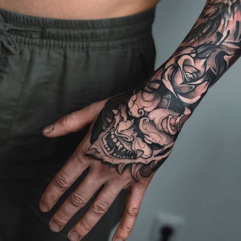 A bold blackwork tattoo extending from the forearm onto the hand, with dense details and a strong graphic look.