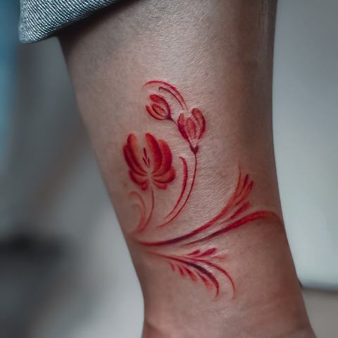 Subtili raudonų tulpių tatuiruotė ant čiurnos, išsiskirianti lengvomis linijomis, švelniu spalviniu perėjimu ir elegantiška augaline kompozicija.