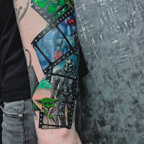 A geometric forearm tattoo with stained-glass inspired shapes and vivid green and blue details