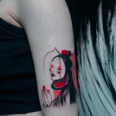 A graphic upper-arm tattoo featuring a stylized female portrait, bold black linework, and vivid red details that give the design a modern, expressive feel.