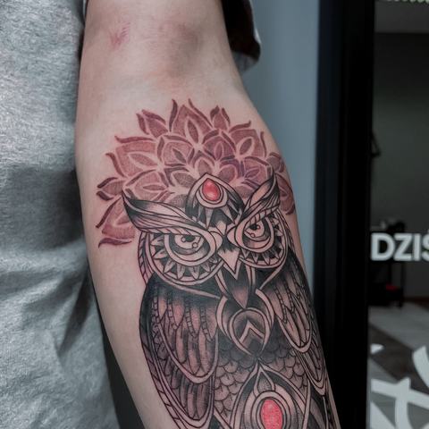 A detailed owl tattoo with ornamental patterns, layered shading and subtle red accents.