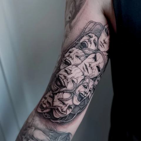 Dinamiška juodai pilka tatuiruotė ant rankos, kurioje detalūs veidų motyvai susilieja į vientisą, kontrastingą kompoziciją su ryškiu charakteriu.