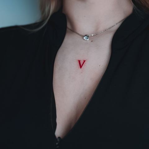 A minimalist red letter tattoo on the chest with a clean, understated look.