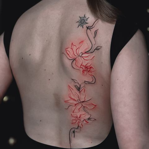 Spalvinga nugaros tatuiruotė su subtiliais raudonais augaliniais motyvais ir smulkiomis simbolinėmis detalėmis, išdėstytomis vertikaliai palei stuburą.