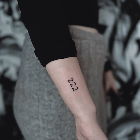 Maža minimalistinė tatuiruotė ant dilbio, sudaryta iš smulkių juodų simbolių, kurie sukuria lakonišką ir vizualiai lengvą kompoziciją.