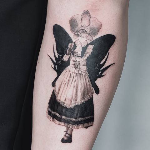 Išraiškinga juodai pilka tatuiruotė su sparnuotos mergaitės figūra, subtiliai papildyta karūnos motyvu ir smulkiomis dekoratyvinėmis detalėmis.