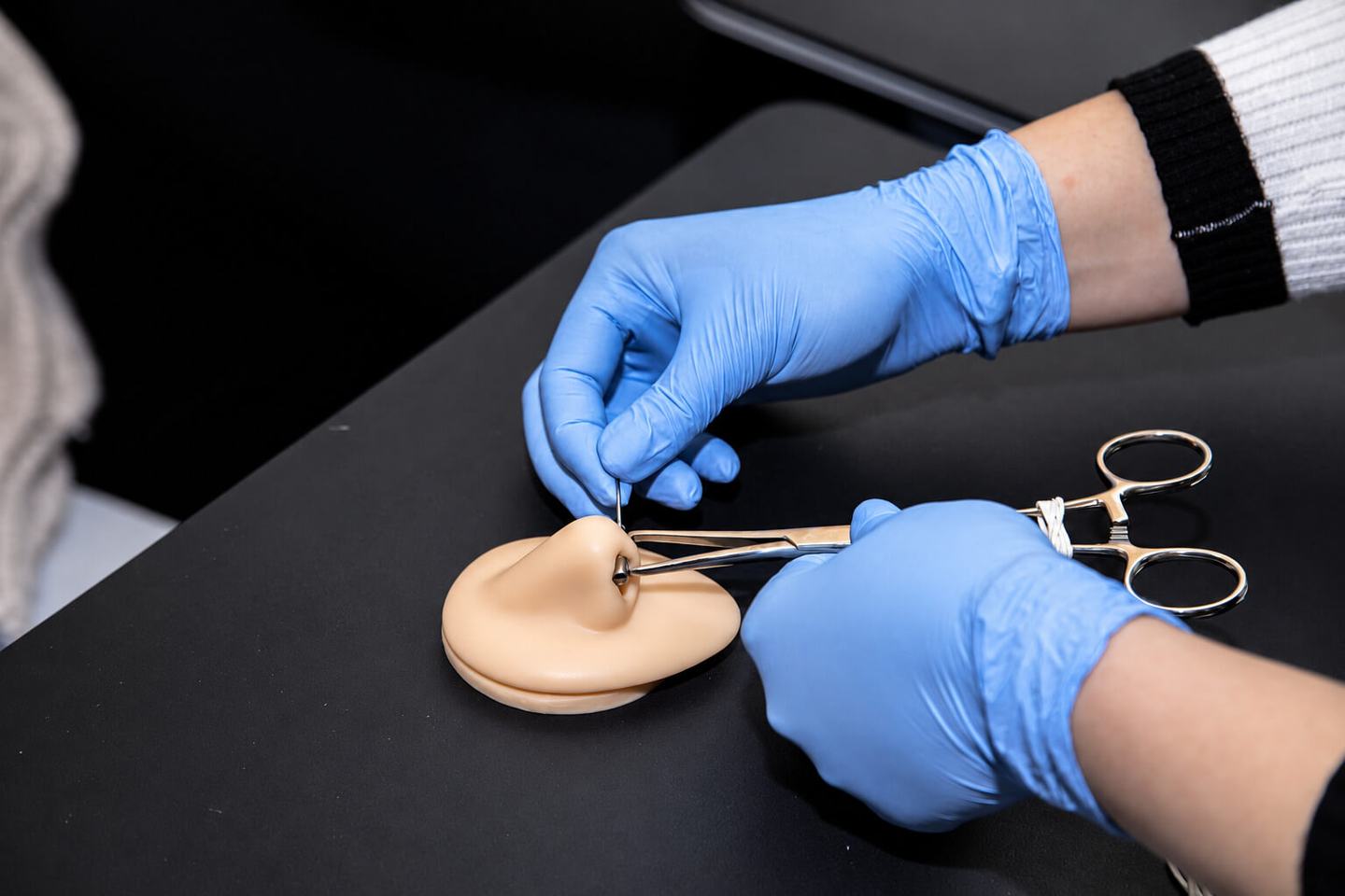 Piercing trainee wearing blue gloves practising on a silicone nose model