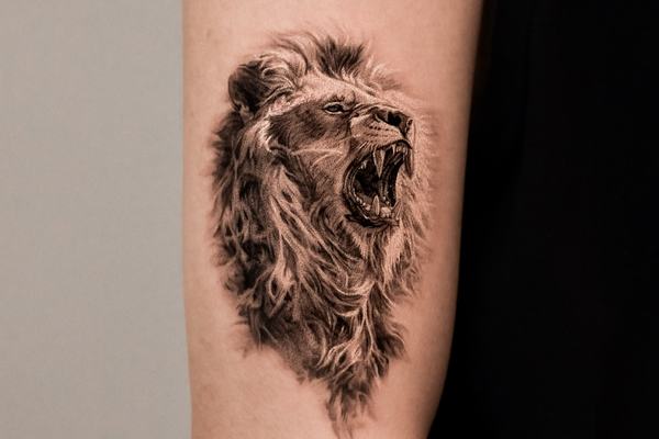 Roaring lion tattoo on forearm in black and grey