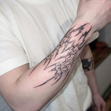 Abstract black tattoo on the forearm with sharp flowing details